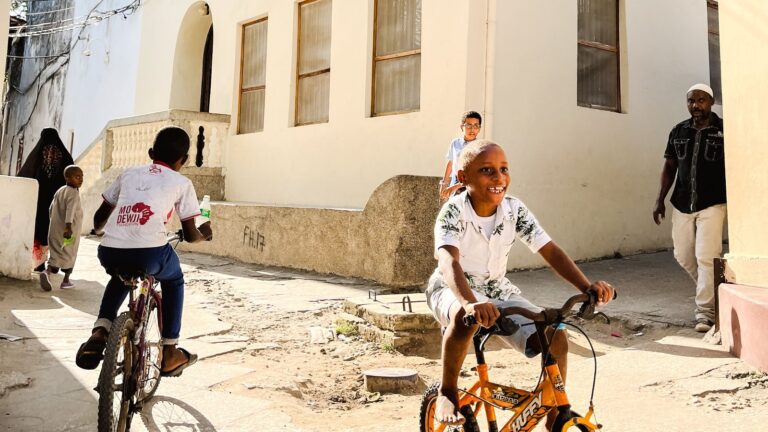 Children riding bicycles through a sunlit Stone Town alley in Zanzibar